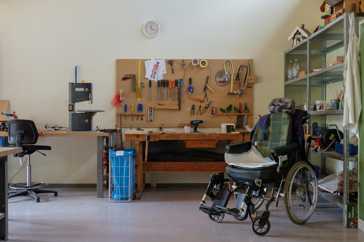 Ein Rollstuhl steht vor einer Werkbank, an der Wand hängt eine Vielzahl von Werkzeugen.