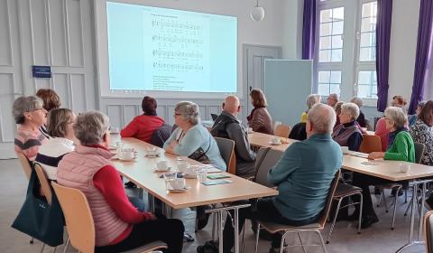 Menschen in einem Raum an Tischen vor einer Leinwand