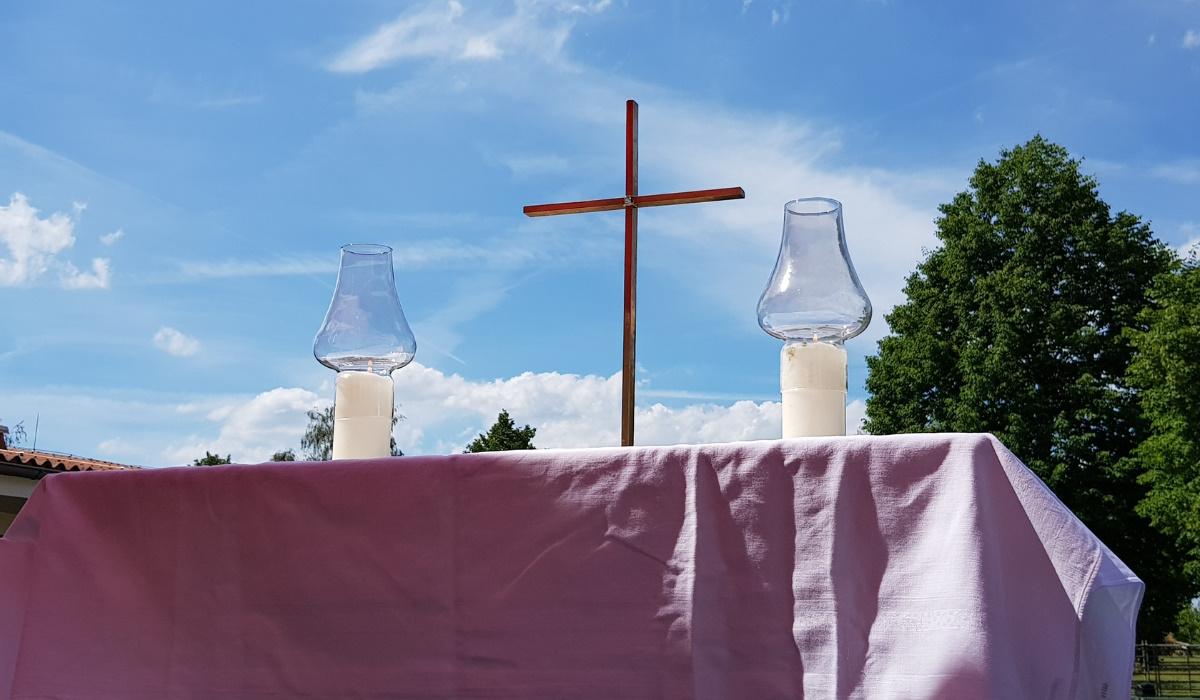 Tisch mit zwei Kerzen und einem Kreuz in der Mitte vor blauem Himmel