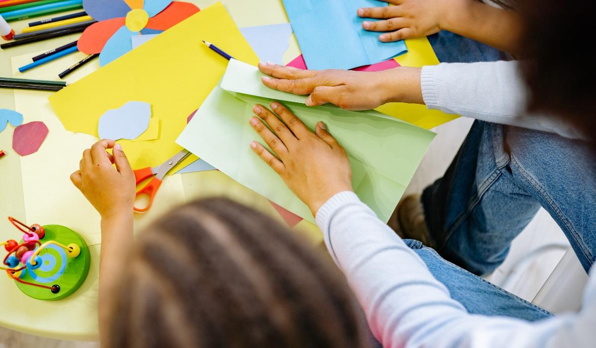 Tisch mit bunten Blättern, Stiften und Kinderhänden